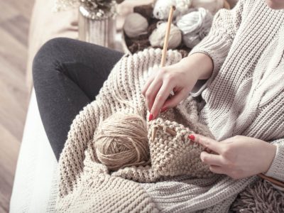 Vintage wooden knitting needles and yarn in woman’s hands Vintage wooden spokes and yarn in the hands of a woman on a cozy sofa . Still life photo. The concept of comfort